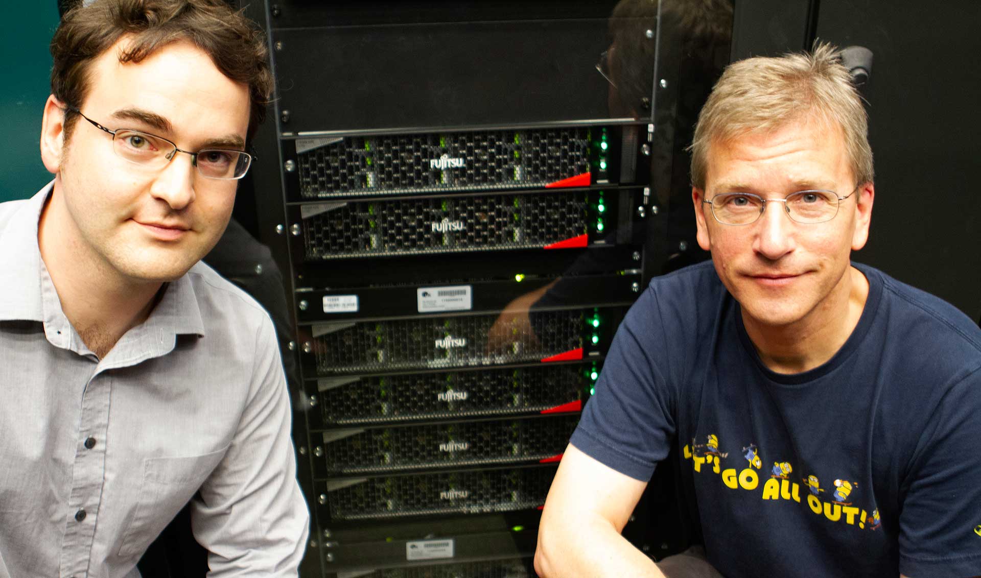 Prof. Dr. Christoph Lehner (links) und Prof. Dr. Tilo Wettig (rechts) vor neuem Supercomputer (Foto: © Christina Glaser)